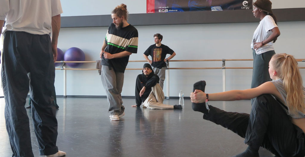 Mains nouant des lacets de baskets de danse sur un sol en bois usé, en noir et blanc avec lumière naturelle rasante